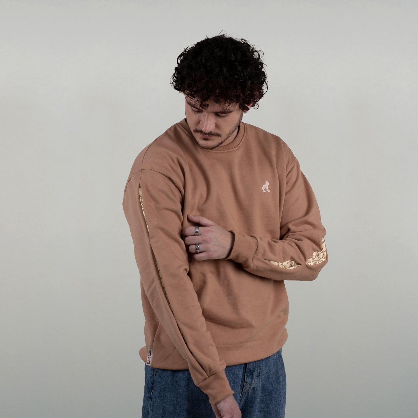 le sweat est vu de 3/4 face, porté par un model masculin, qui met en avant les ouvertures des manches quasiment invisibles une fois le bras tendu