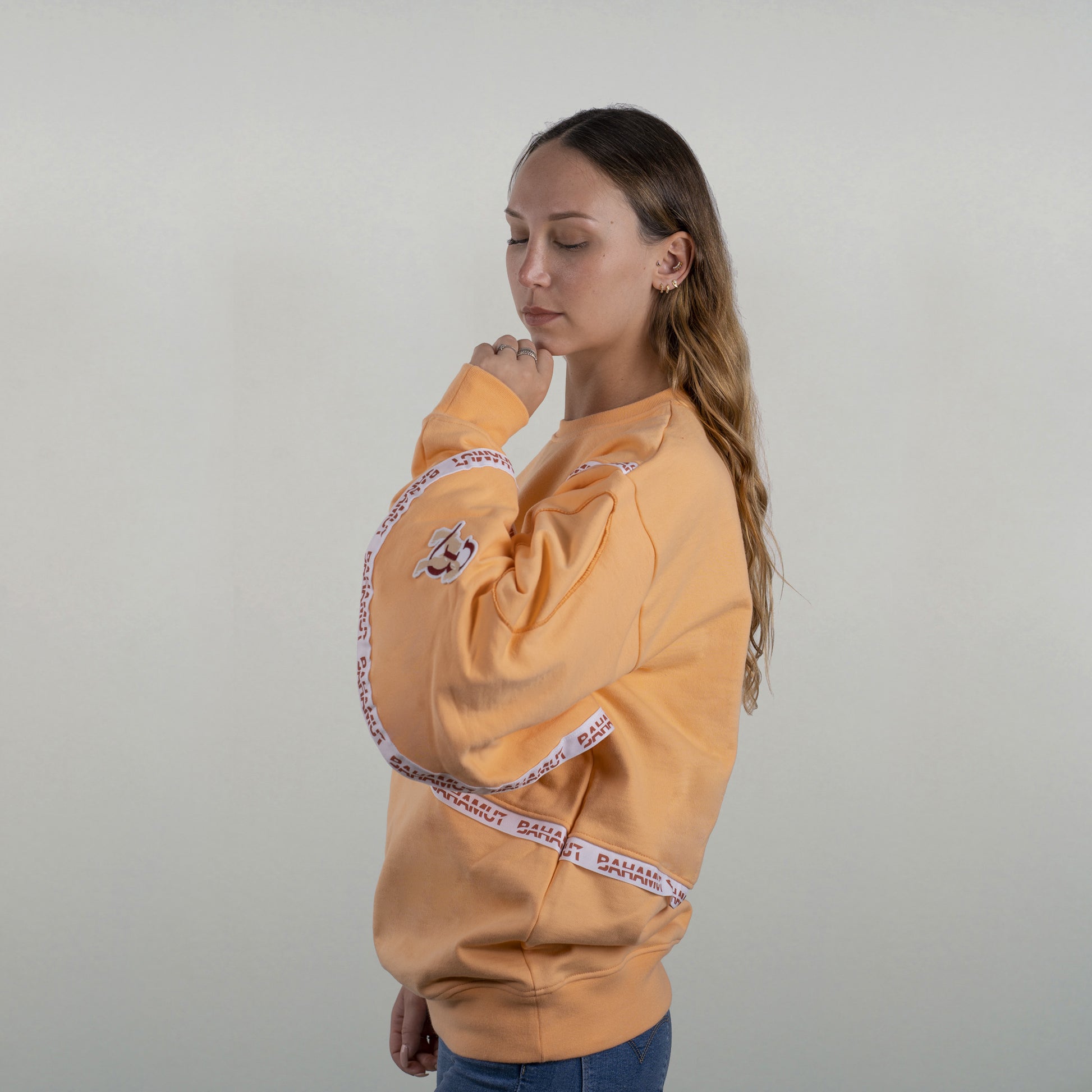 Le sweat porté par un model féminin, vu de profil. La sur-manche et la broderie du blason Bahamut sont bien visibles